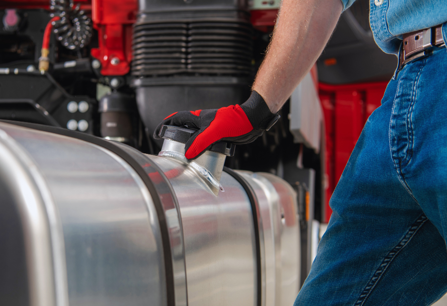 Worker wearing protective gloves inspecting the fuel tank cap on a commercial truck during a maintenance check.